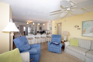 A living room with a sofa, armchairs, a dining area with chairs, a ceiling fan, and a kitchen in the background. - Comfortable 2 bedroom oceanfront condo with free WiFi, an outdoor pool, and balcony with an amazing ocean view located midtown just steps to the beach! (Ocean City)