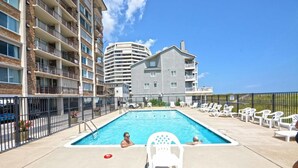 Una piscina con sillas de descanso y un edificio con varios balcones al fondo.
