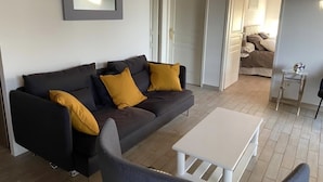 Ein modernes Wohnzimmer mit einem dunkelgrauen Sofa, gelben Kissen, einem weißen Couchtisch und einem Spiegel an der Wand.
