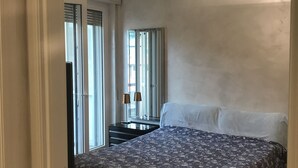 Een slaapkamer met een bed, een kastje, een spiegel en een raam met zonwering.