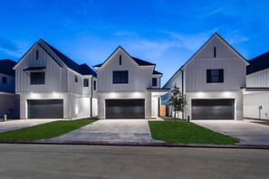 Une rangée de maisons modernes à un étage, dotées de garages attenants, de pelouses bien entretenues et surplombées par un ciel dégagé.