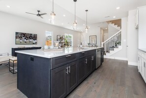 Una cocina moderna con muebles oscuros, una isla grande, iluminación colgante y una escalera que sube a un nivel superior.