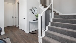 Un escalier avec une rampe blanche et des marches recouvertes d’une moquette grise, menant à un palier.