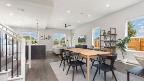 Un vaste espace de vie comprenant une grande table à manger en bois, des chaises noires et un escalier moderne.