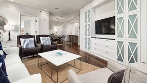 A modern living room with a white sofa, a coffee table, and a TV mounted on a white cabinet with glass panels.