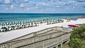 A beach with rows of umbrellas and chairs, a wooden walkway, and a view of the sea.