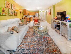 A living room with a white sofa, a glass coffee table, and a colorful rug.