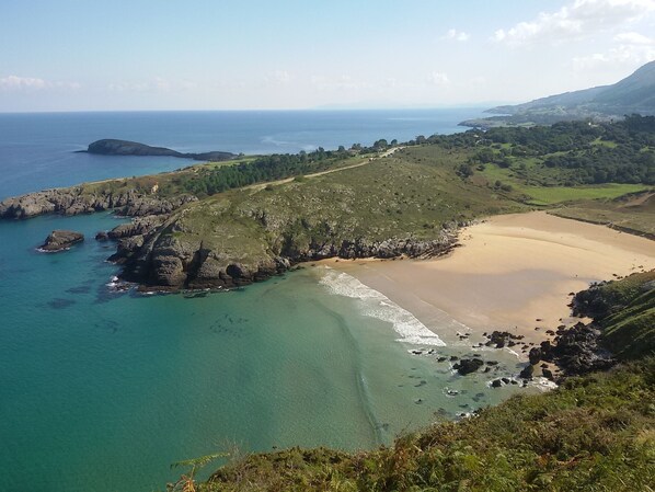 Un paisaje costero con playa, costa rocosa y colinas al fondo.