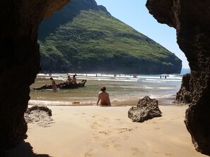 Una playa con la entrada de una cueva, orilla de arena y una montaña al fondo.