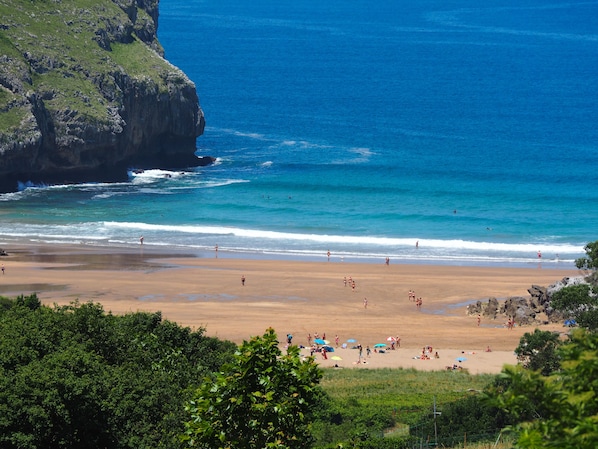 A beach with clear blue water, a sandy shore, and rocky cliffs.