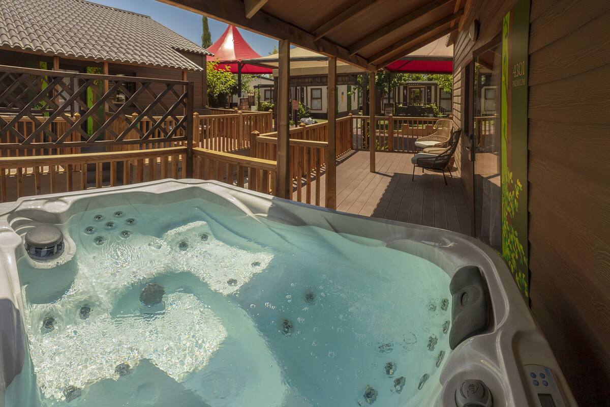 A hot tub with a wooden deck and a view of a building with a red roof.