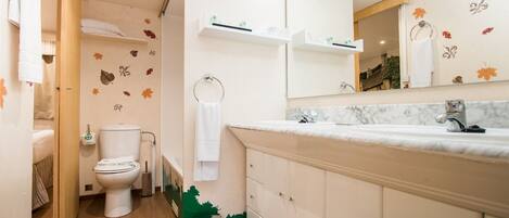 A bathroom with a toilet, sink, mirror, and storage cabinets.