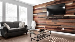 A modern living room with a wooden wall panel, a flat-screen TV, a glass coffee table, and a dark-colored sofa. - Stunning & Spacious home, 8 beds, PS4, Karaoke and lots more! (Spring)