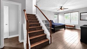 A spacious room with a wooden staircase, a bed, a bench, and a ceiling fan. - Stunning & Spacious home, 8 beds, PS4, Karaoke and lots more! (Spring)