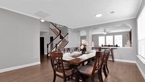 A dining area with a wooden table set for six, surrounded by chairs. A staircase with a railing leads to an upper level. - Stunning & Spacious home, 8 beds, PS4, Karaoke and lots more! (Spring)