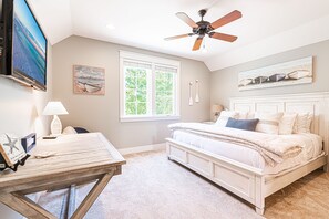 Une chambre à coucher avec un lit, un ventilateur de plafond, une fenêtre et un téléviseur fixé au mur.