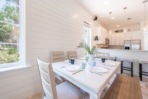 Un coin repas avec une table blanche dressée pour quatre personnes, entourée de chaises en bois.
