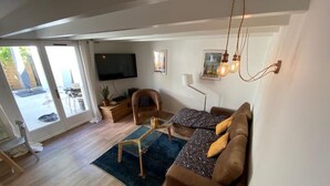 Amplia sala de estar con sofá, una mesa de centro y televisor. Hay un ventanal y una puerta que da a un espacio exterior.