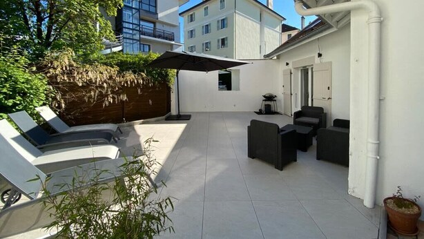 Un patio moderno al aire libre con zona de estar, una pérgola y vistas a edificios cercanos.
