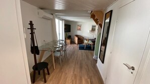Una habitación con piso de madera, una mesa de vidrio con sillas, una guitarra apoyada contra la pared y una puerta con espejo.