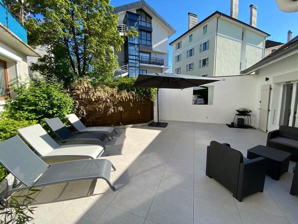 Un espace extérieur aménagé en terrasse, avec des chaises longues et une table à manger, entouré d’un petit muret et d’un grand parasol.