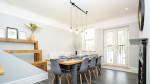 A modern dining area with a wooden table and chairs, a hanging light fixture, and a view of the outdoors through large windows. - 4 bed seaside let with parking
Central Broadstairs (Broadstairs)
