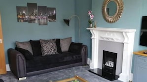 A living room with a dark-colored sofa, a white fireplace, and a coffee table. - 4 bed seaside let with parking
Central Broadstairs (Broadstairs)
