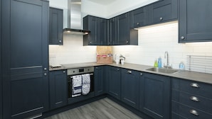 A modern kitchen with dark blue cabinets, a stainless steel range hood, a built-in oven, and a sink with a soap dispenser. - 4 bed seaside let with parking
Central Broadstairs (Broadstairs)
