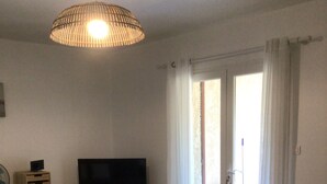 Un comedor con una mesa, sillas, un televisor sobre un soporte y una lámpara de techo.
