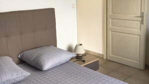 Un dormitorio con dos camas, una mesita de noche con lámpara y una puerta.