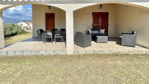 Un espacio al aire libre cubierto con mobiliario de mimbre y una mesa, bajo un techo de tejas y una pared de piedra.