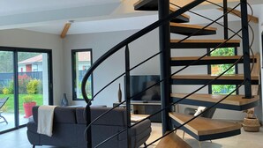 A modern spiral staircase with a minimalist design, a grey sofa, and a TV in a spacious living area with large windows. - La Villa des Pins 150 m2 at 5 min from the beach with 3 bedrooms and 8 beds (Messanges)