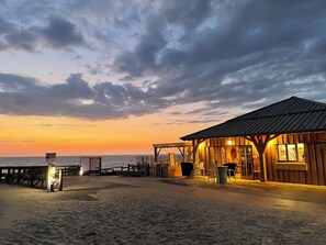 A wooden building with a metal roof, located on a sandy beach with a view of the ocean.