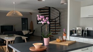 A modern kitchen with a central island, bar stools, a dining area with a TV, and a spiral staircase. - La Villa des Pins 150 m2 at 5 min from the beach with 3 bedrooms and 8 beds (Messanges)