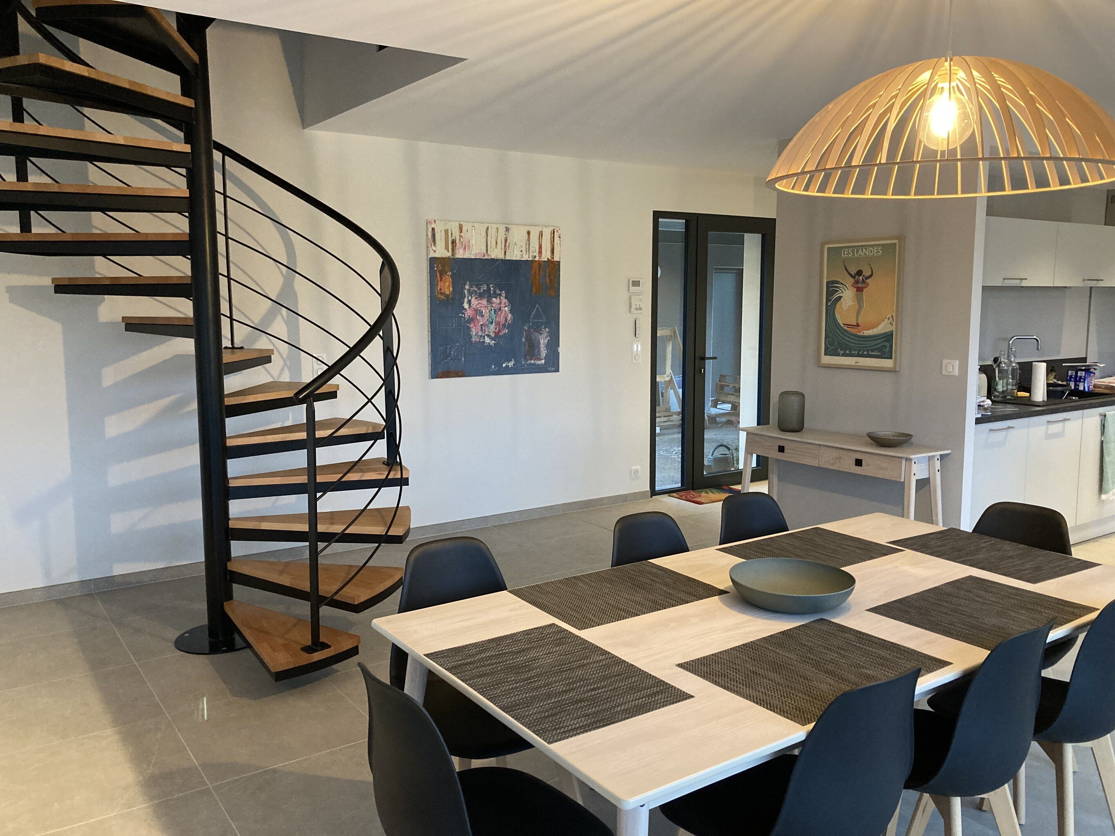 A modern kitchen with a dining area, featuring a spiral staircase, a large dining table with chairs, and a pendant light.