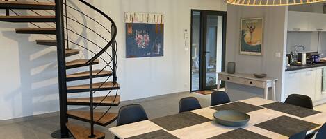 A modern kitchen with a dining area, featuring a spiral staircase, a large dining table with chairs, and a pendant light.