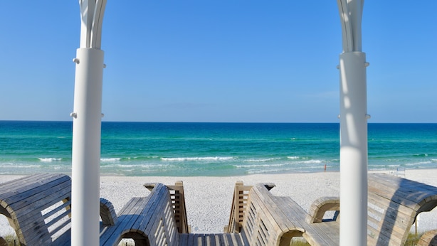 Ein Strand mit hölzernen Bänken und einem weißen Gazebo mit Blick aufs Meer.