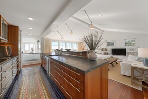 A modern kitchen with a large island, wooden cabinetry, and a tiled floor.