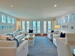 A spacious living room with white furniture, large windows, and a blue carpet.