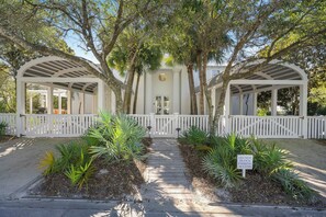 A covered walkway leading to a white building with a white picket fence, surrounded by palm trees.