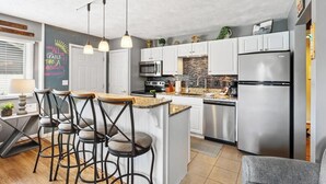 Una cocina moderna con una isla central, taburetes de bar, electrodomésticos de acero inoxidable y una pizarra con mensajes motivadores.