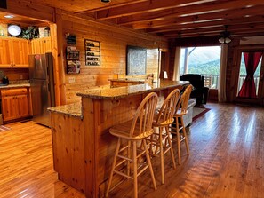 A wooden cabin interior with a kitchen area featuring a granite countertop, wooden bar stools, and a refrigerator.