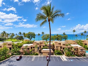 A hotel with multiple-story buildings, a parking lot, and a view of the ocean.
