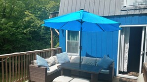 A deck with wicker furniture, a blue umbrella, and a view of the surrounding forest.