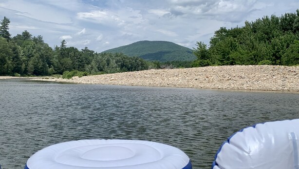 A river with a rocky shore and a forested hill in the background.