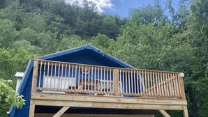 A blue cabin with a wooden deck and a staircase leading to a second-floor balcony.