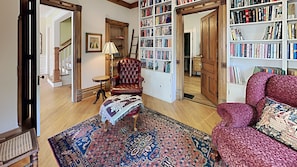 Un salón acogedor con un sillón rojo, una alfombra estampada y una estantería llena de libros.