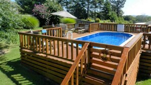 Une piscine rectangulaire dotée d’une terrasse et d’une rambarde en bois, entourée de verdure et d’arbres.