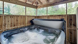 Un bain à remous avec une terrasse en bois et une vue sur les arbres à travers les fenêtres.