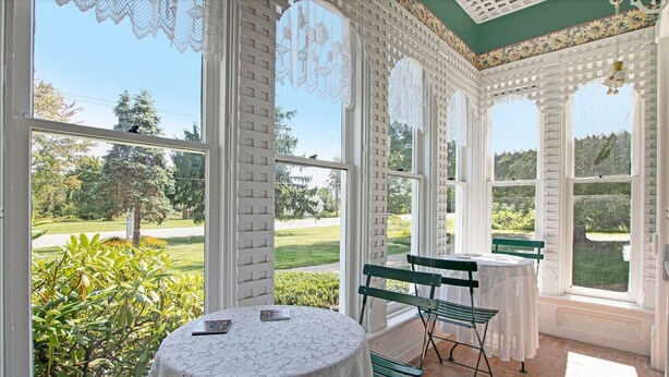Une véranda avec une table ronde et deux chaises, de grandes fenêtres et une vue sur un jardin.